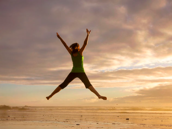Woman jumping up in air with arms and leg extended on beach